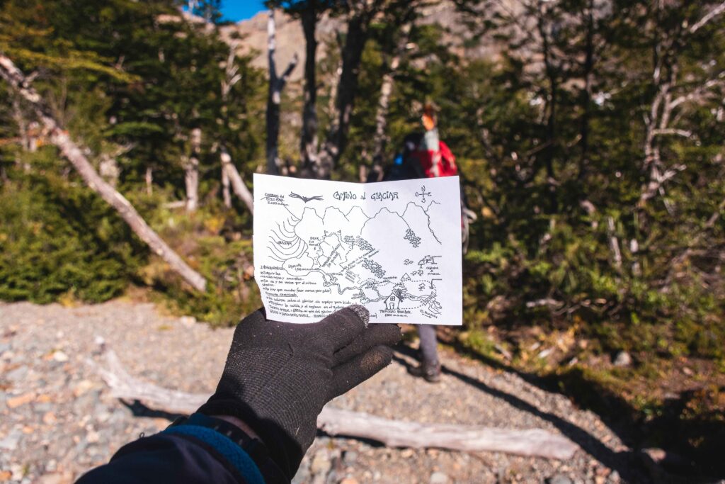 "Mano sosteniendo un mapa en medio de las montañas, mientras una persona planifica su viaje